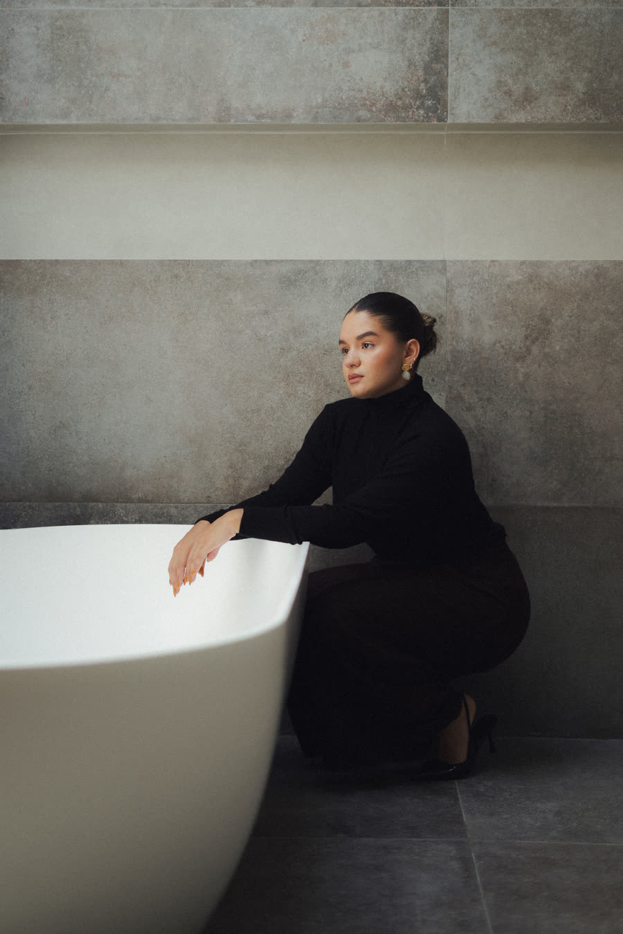 Mafer González arrodillada junto a una bañera, con suéter negro