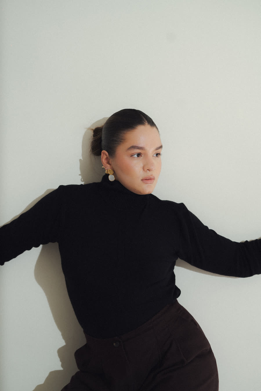 Mafer González de perfil, con suéter negro, apoyada en una pared clara